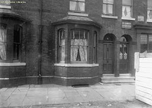 Black and white shot of a terraced house with net curtain.